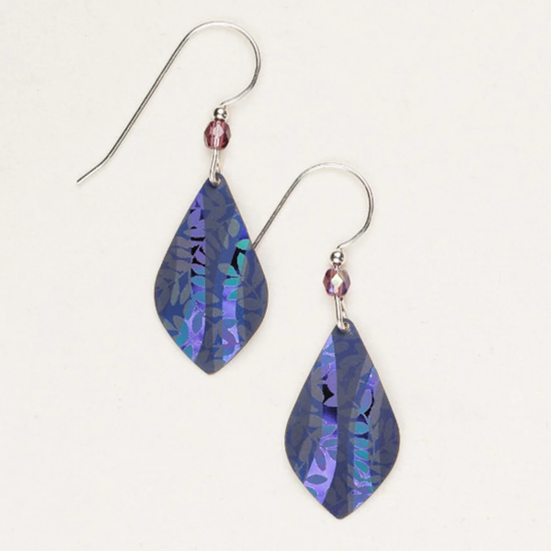 A pair of Holly Yashi Riverwind Earrings featuring iridescent, leaf-shaped pendants in a dark purple and blue pattern. The earrings, epitomizing botanical beauty, are attached to hooks adorned with small crystal beads on an off-white background.