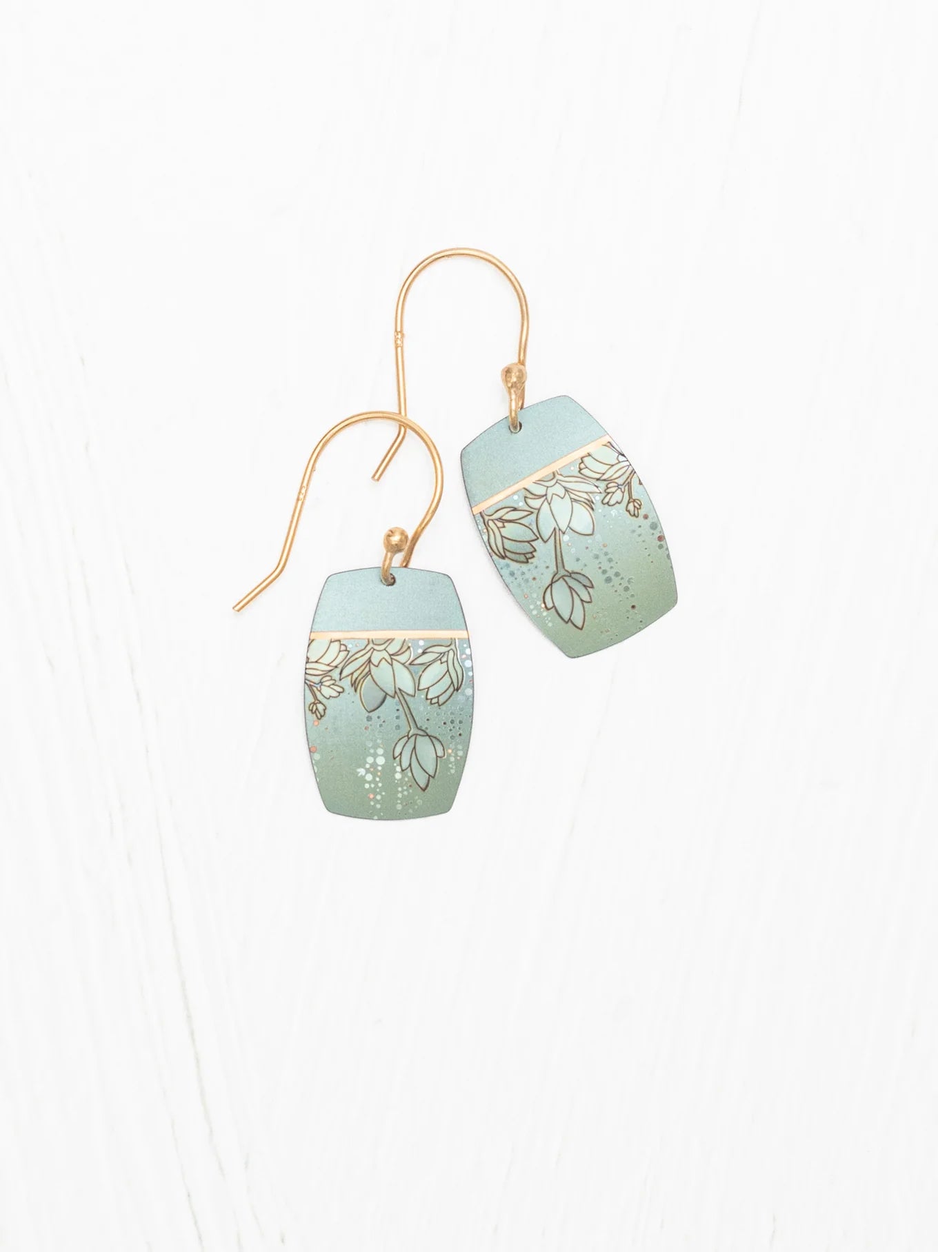 A pair of Holly Yashi Cari Earrings with a gold hook. The rectangular dangle earrings feature a light green gradient background adorned with delicate white floral illustrations and gold accents, reminiscent of ocean blues jewelry. These tropical floral earrings are displayed on a white surface.