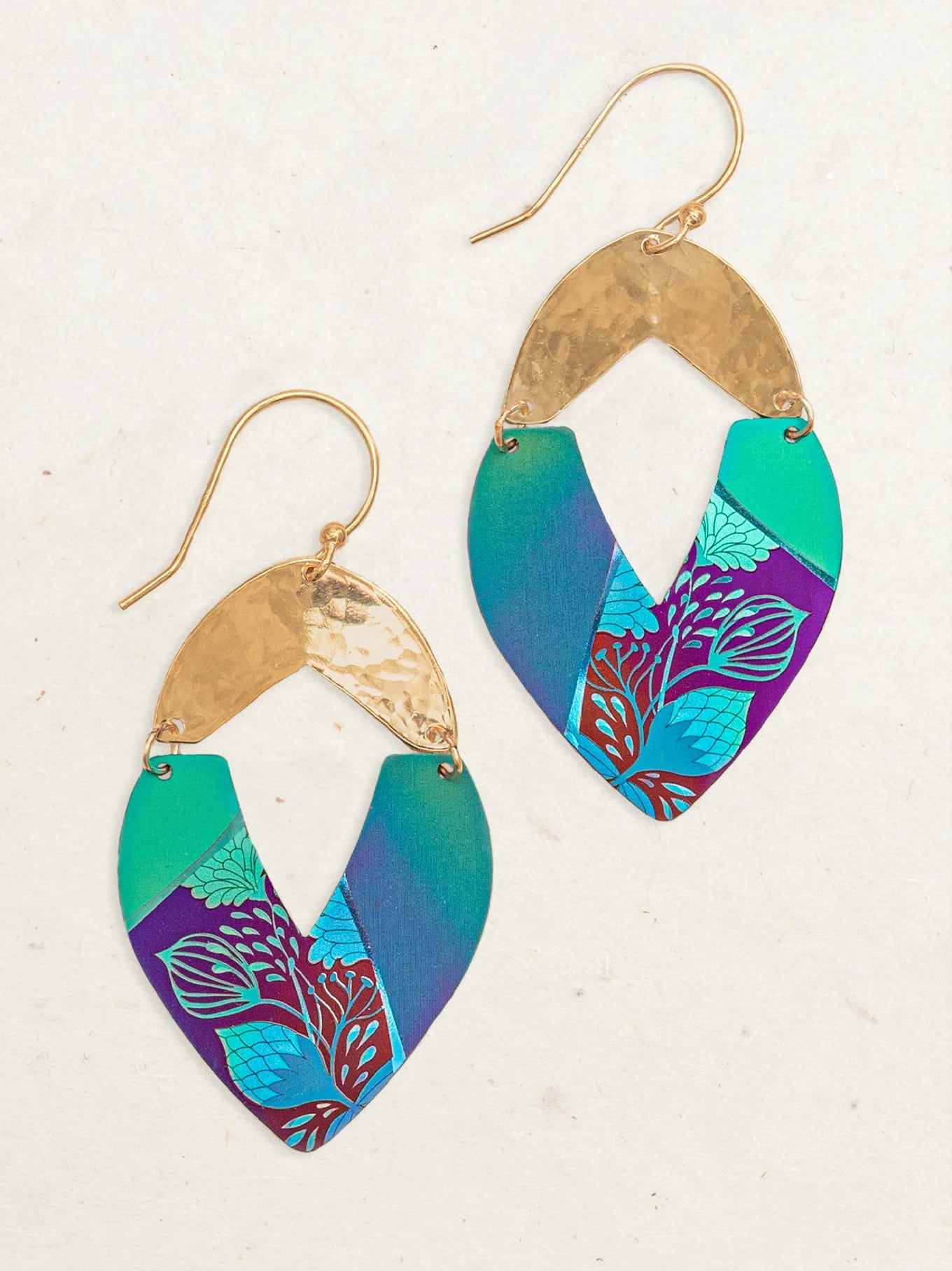 Introducing the Holly Yashi Kalea Earrings: a pair of stylish drop earrings with gold hooks. These earrings feature hammered gold accents at the top and showcase layered, teardrop-shaped pieces in vibrant turquoise, blue, and purple tones with intricate leafy patterns, reminiscent of island florals.