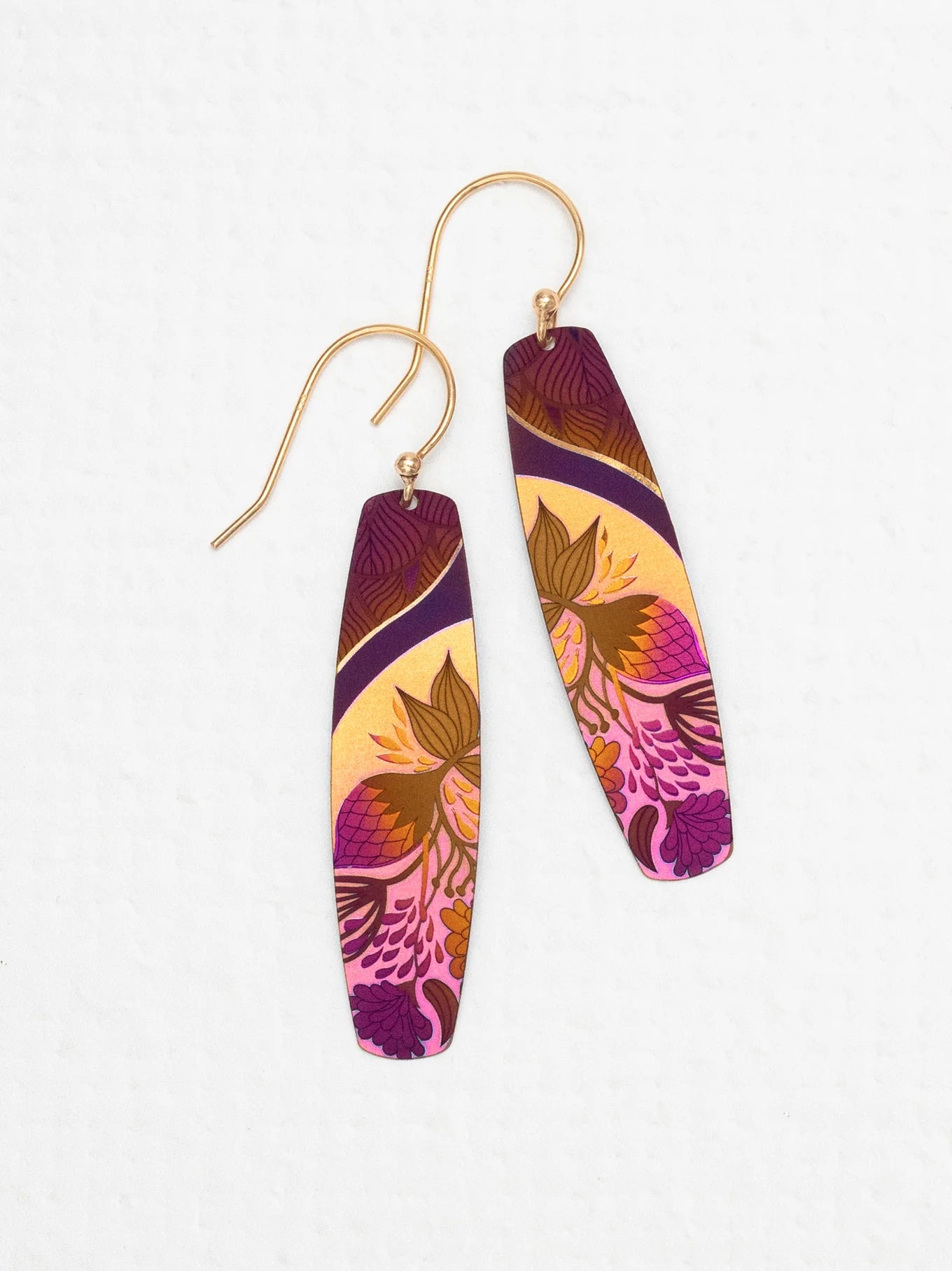A pair of Holly Yashi Malia Earrings with golden hooks showcases a vibrant, intricate design in shades of purple, pink, yellow, and brown. The 18K Gold-plated Niobium enhances the tropical florals and abstract elements, creating a bold and artistic look. The earrings are laid out on a white background.