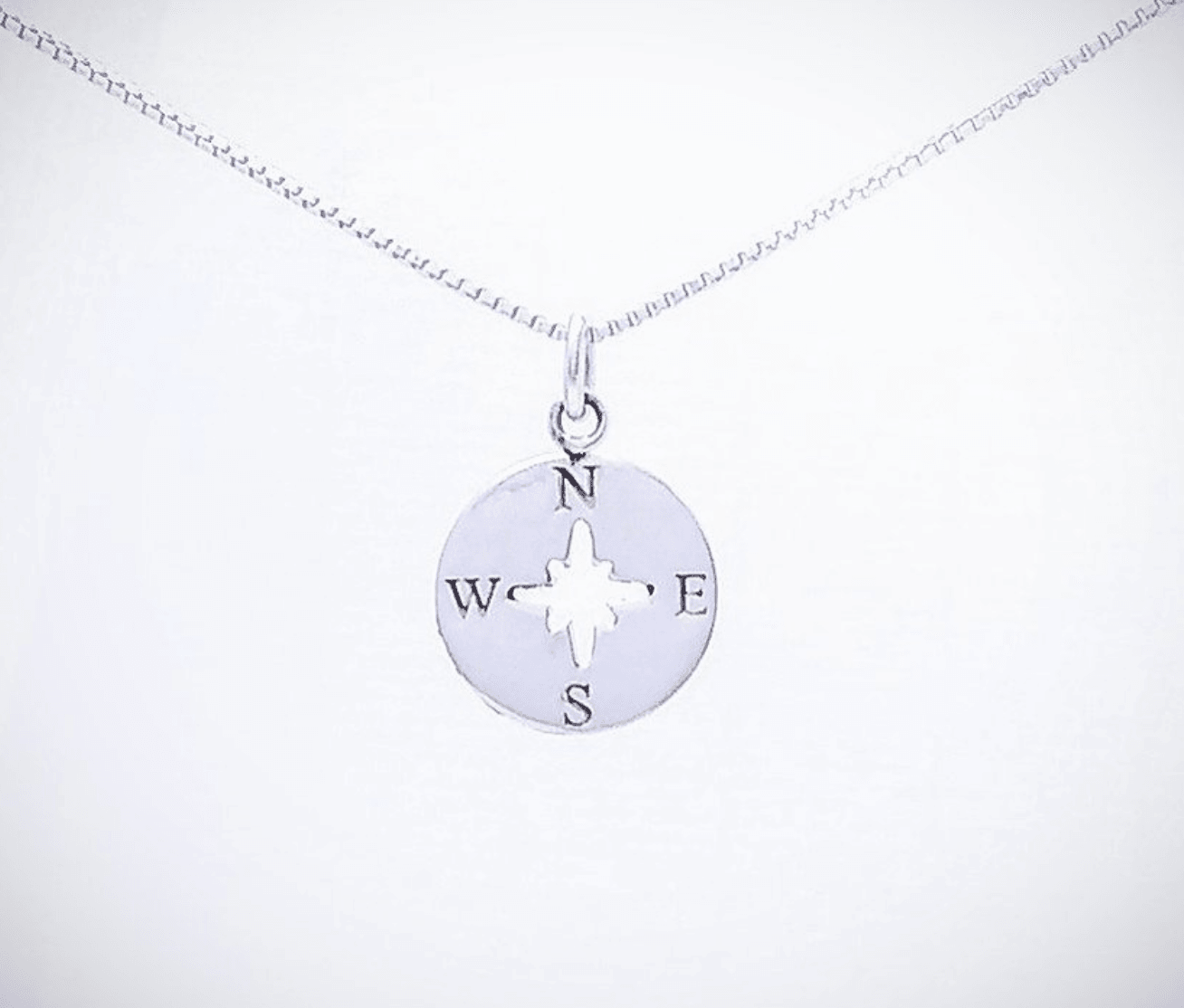 A small circular compass pendant with a cutout in the center pointing to the cardinal directions noted with their letters