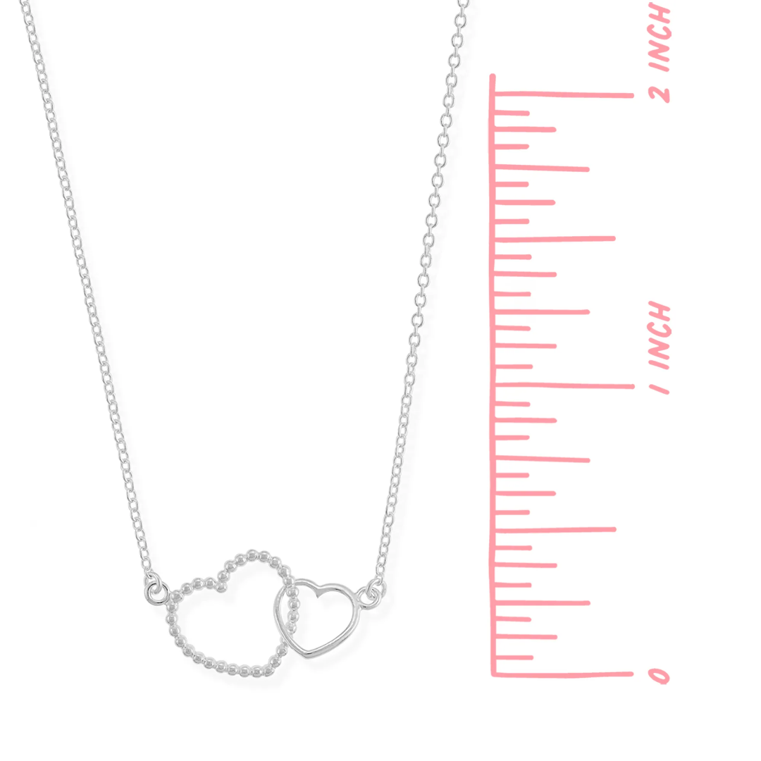 Interlocking heart necklace on white background, one heart bigger than the other, bigger heart is textured while smaller heart is smooth; on a thin silver chain. Hearts measure approx. .25 inches tall and wide.