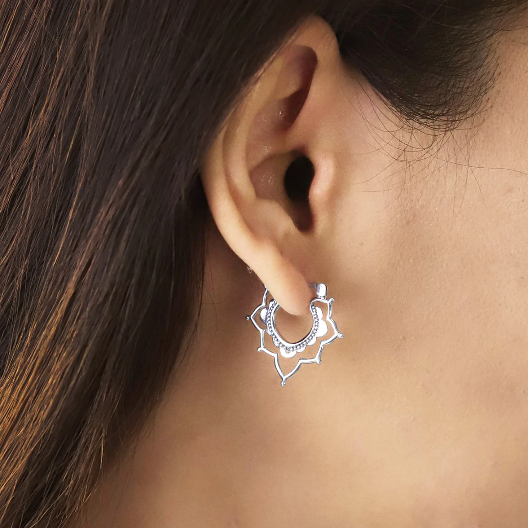 Snap top lotus-shaped silver hoop on human ear.