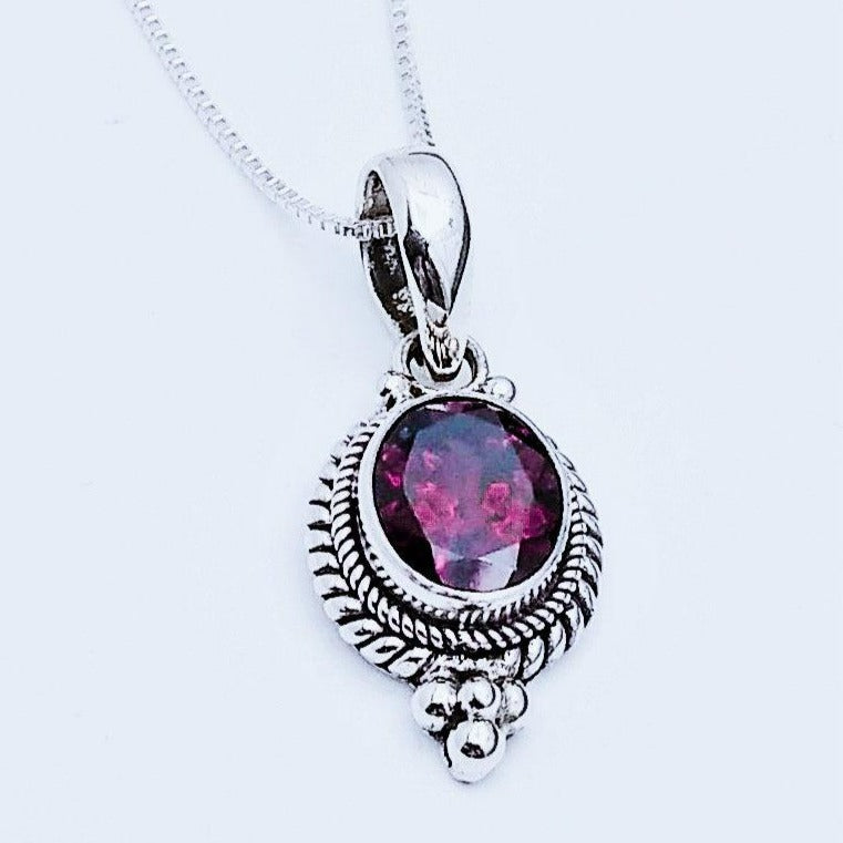Sterling silver pendant with woven rope design along the sides, with three small silver balls at the top arranged in a triangular fashion. In the middle is a Garnet stone. Comes on an 18-inch chain. January birthstone