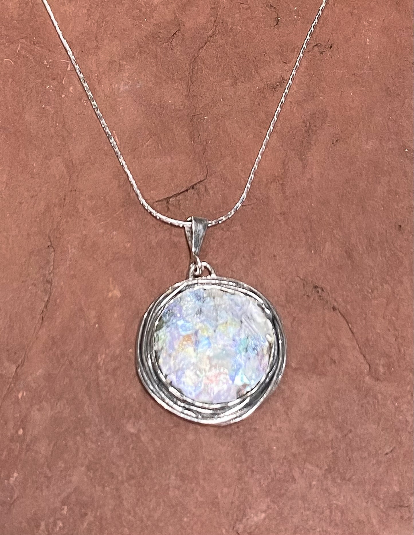 1 inch diameter piece of 2000 year old Roman glass set in an ornate Sterling Silver Bezel. Includes 18 inch chain.