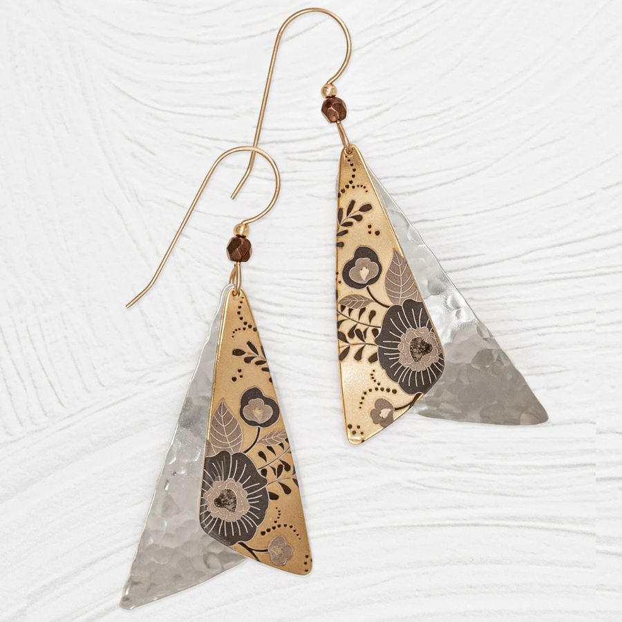 The Holly Yashi Forever Flutter Earrings showcase hand-crafted elegance with their stunning pair of triangular dangle designs in gold and silver tones. The intricate floral and leaf patterns on the gold section feature detailed etchings, while the silver section boasts a textured, hammered finish. Each earring is beautifully accented with a small brown bead at the top.