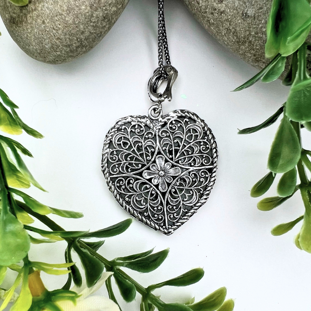 Backside of large Roman Glass heart necklace - the back is an intricate floral design hand-stamped out of 925 Sterling Silver with a braided border. 