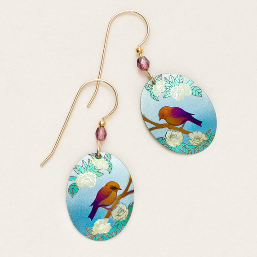 Holly Yashi Birdsong Earrings - Ovular flat Holly Yashi earring with a simple design of a purple and gold-colored bird sitting on top of a brown branch with leaves. The background is a gradient light blue sky. The earrings are on a bronze-colored ear wire with a bold purpleish-pink bead at the top.