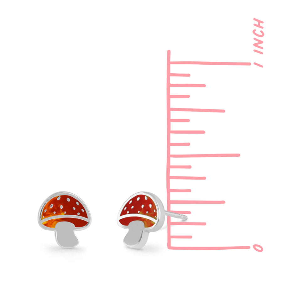 The Boma Mushroom Studs, a pair of small, red-and-white mushroom-shaped stud earrings with sterling silver stems, are placed next to a vertical pink measuring scale, indicating their height is just under one inch. These hypoallergenic earrings beautifully complement the matching necklace.