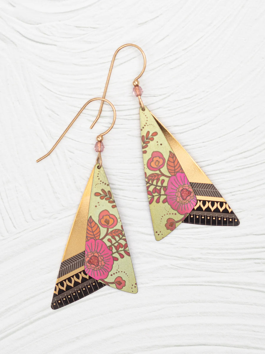 The Holly Yashi All A Flutter Earrings, a stunning example of hand-crafted elegance, feature a pair of triangular dangles adorned with gold, green, and floral patterns. These earrings showcase layered pink and red flowers with geometric accents on hook wires. They are beautifully displayed on a textured white surface.