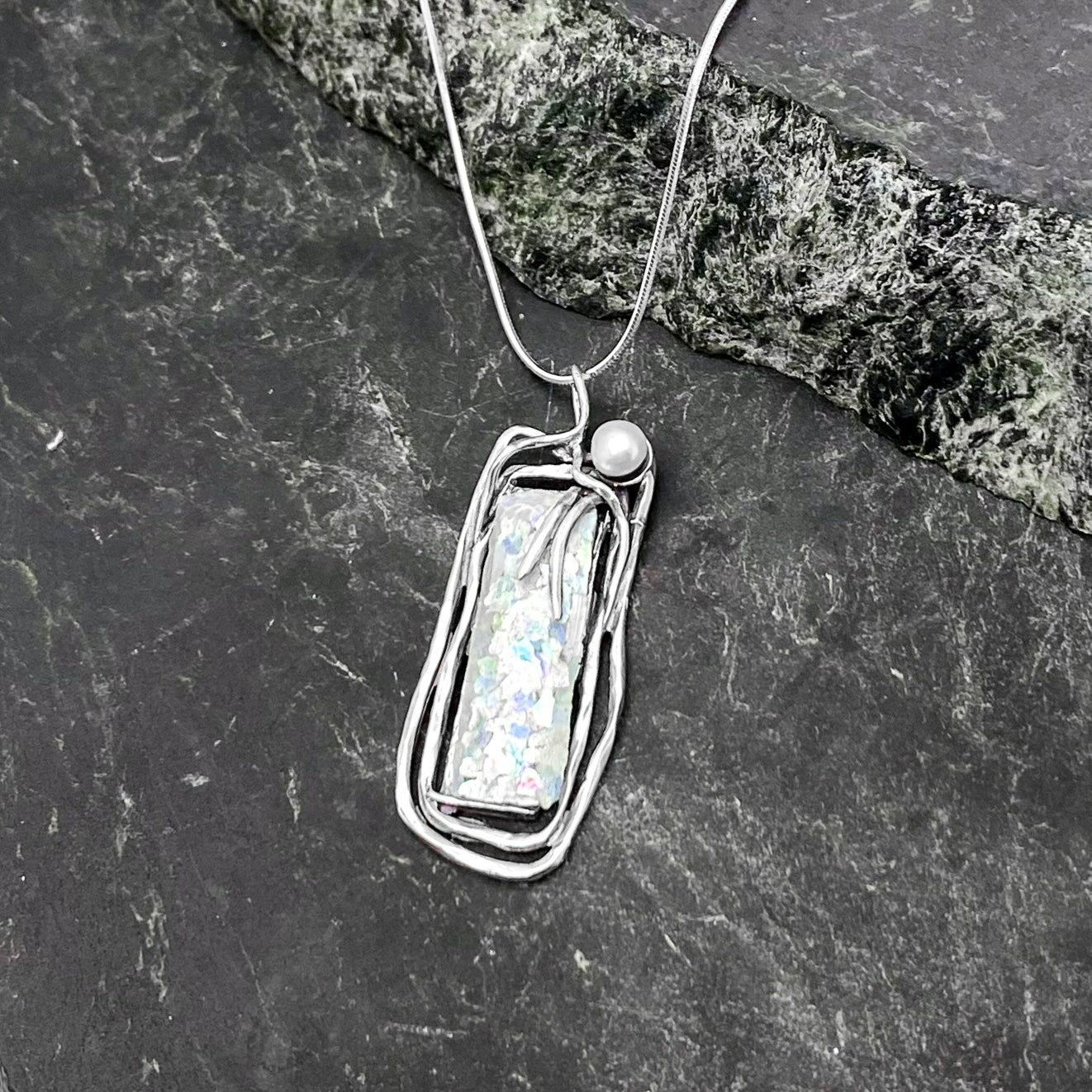 Rectangular Roman Glass suspended in a 925 Sterling Silver vined setting, accompanied by a single white pearl in the top right corner.