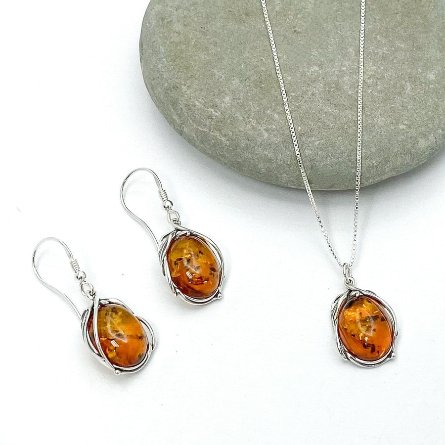 Urban Sterling Silver - Oval shaped Baltic Amber in floral / vine-like 925 sterling silver setting sitting next to matching pendant necklace