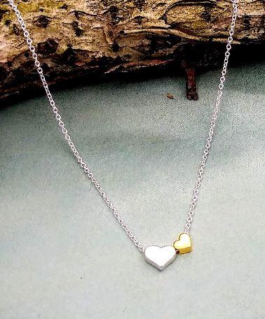 Sterling silver Boma necklace with one silver heart and one smaller gold heart to the right. the chain runs through them.