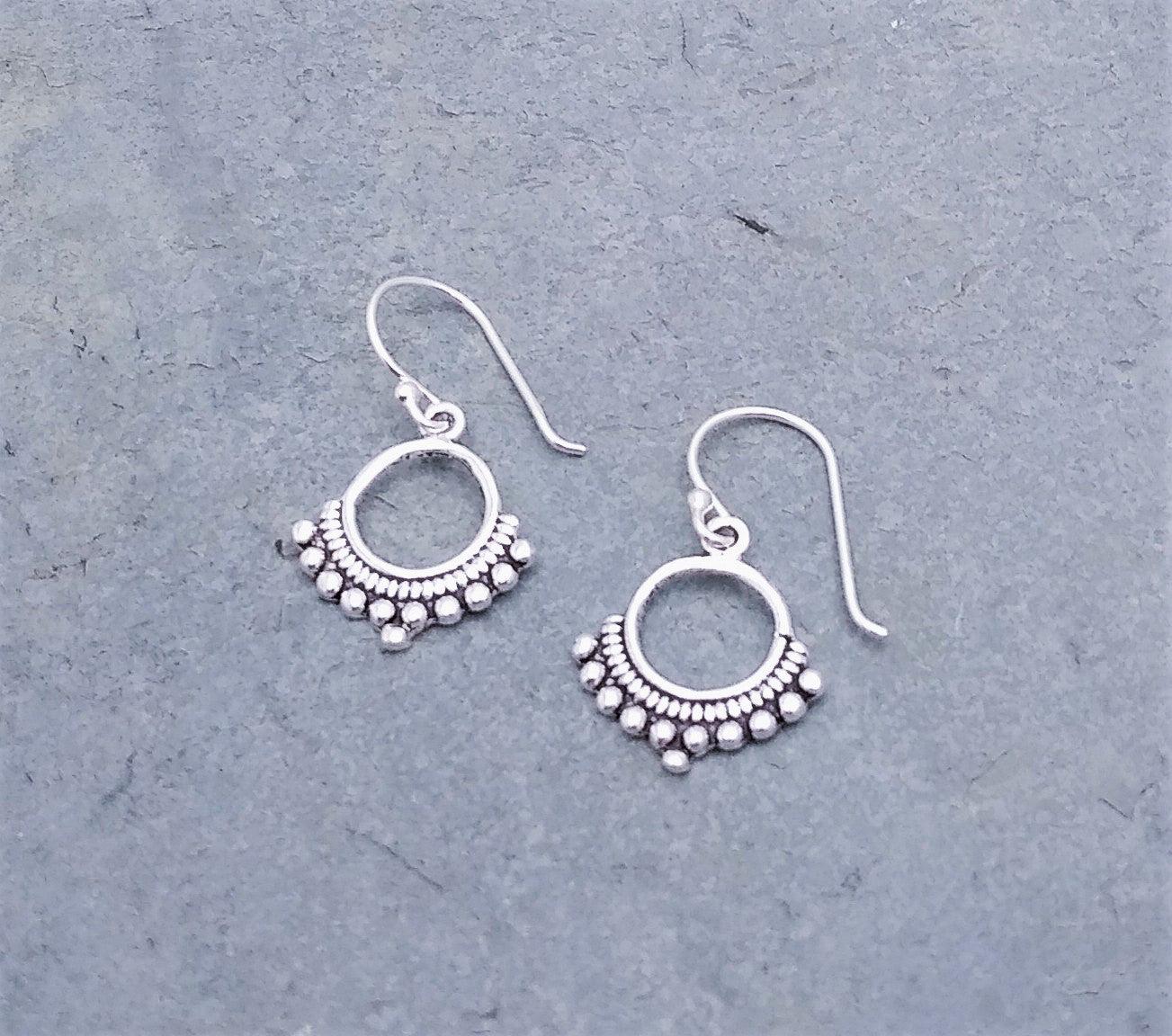 Sterling silver dangle earrings with a circle-cutout middle and a bali design along the bottom. On a french wire