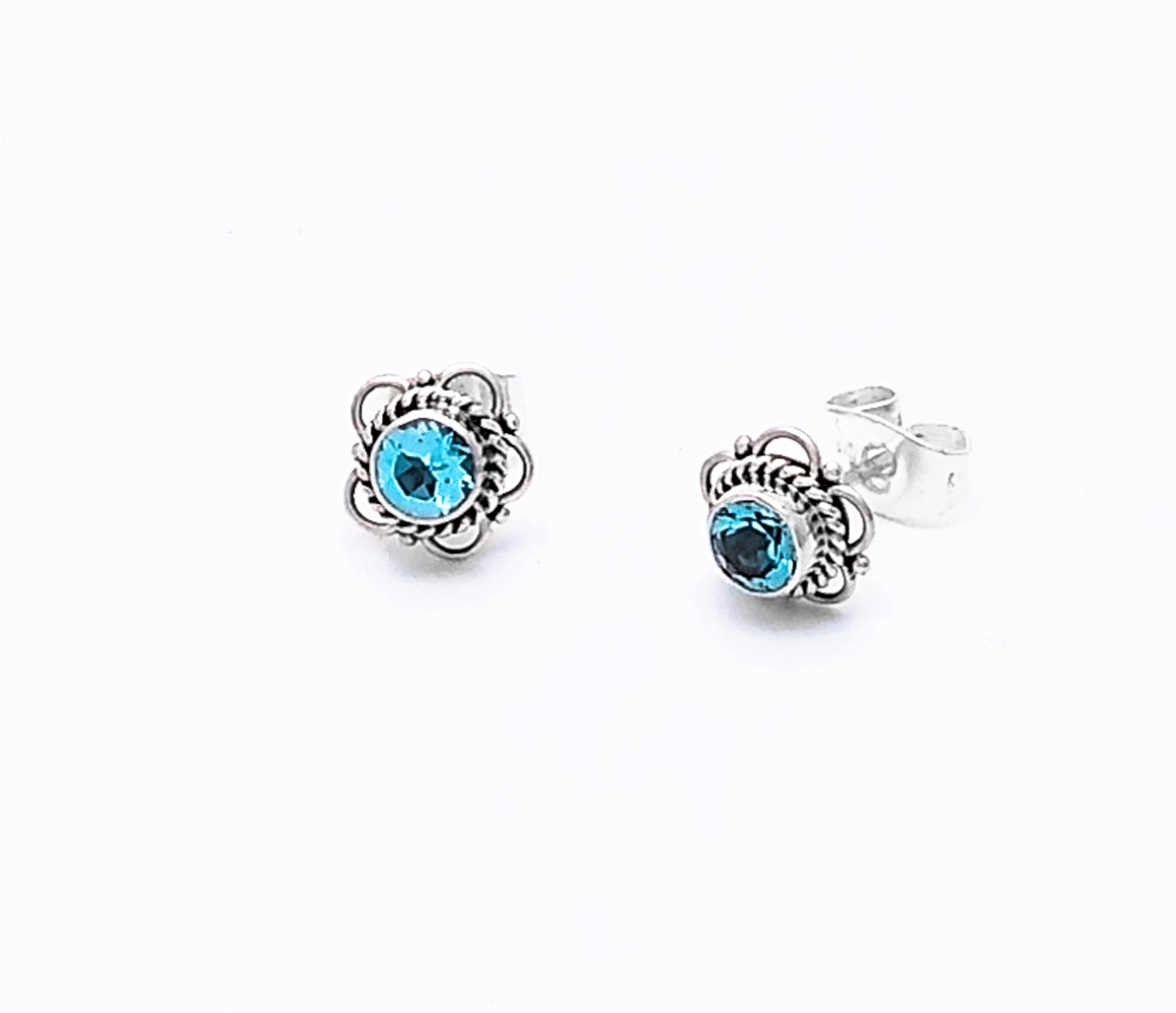 Two Bali Stone Sterling Silver Studs, each featuring a bright blue gemstone at the center of intricate swirled settings, handmade in Bali and displayed against a white background.