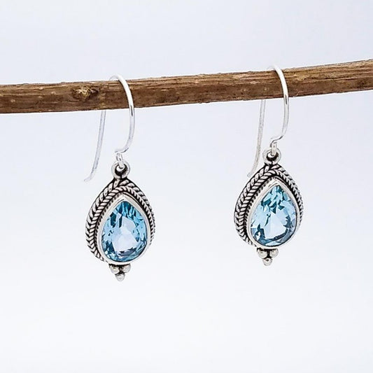 Sterling silver teardrop-shaped drop earrings on a French wire with ornate setting around a Blue Topaz stone in the middle. December birth stone.