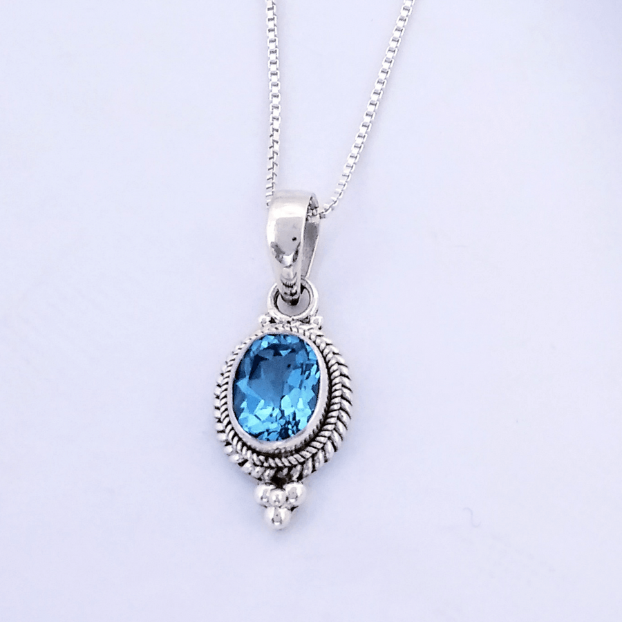 Oval faceted blue topaz in sterling with twist/braid detail around the edge and 4 balls in a pyramid shape at the bottom. A bale connects it to box chain.