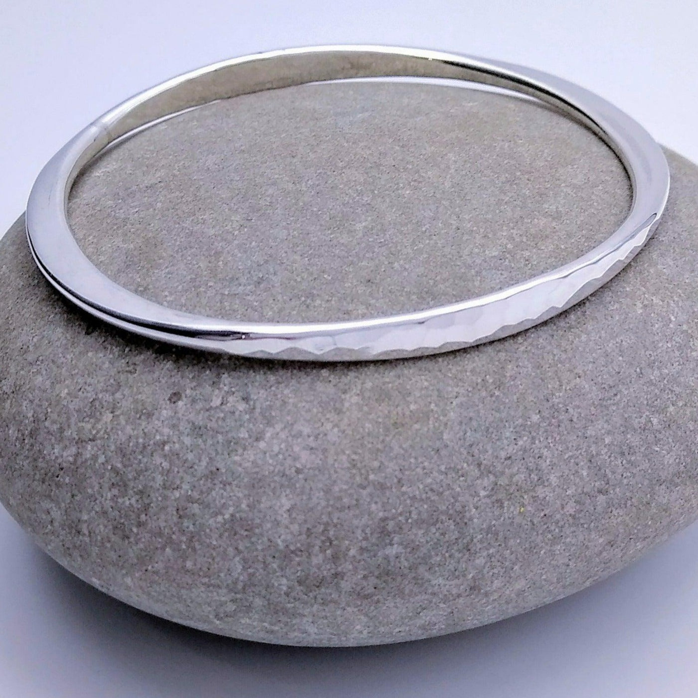 925 Sterling Silver hammered bangle sitting on top of a rock. Two parallel sides are hammered flat.