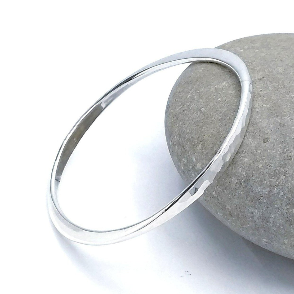 925 Sterling Silver hammered bangle leaning against a rock. Two parallel sides are hammered flat.