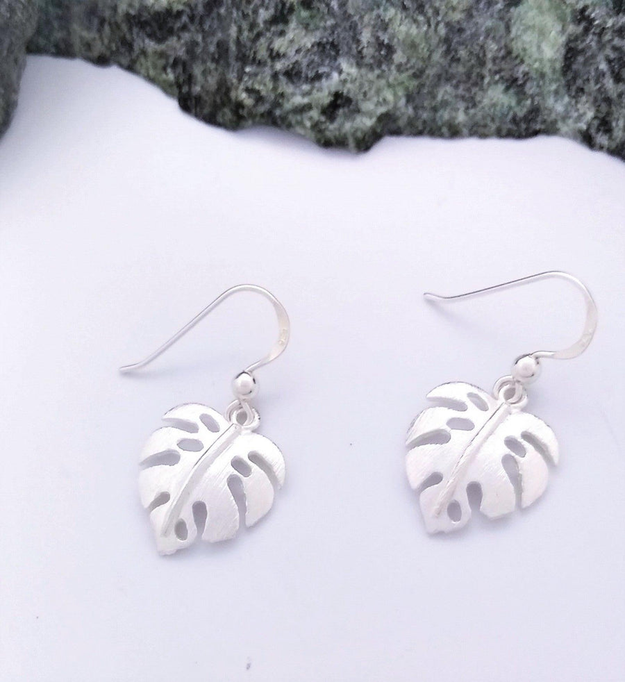 Matted silver dangle earrings of monstera leaves with center line and 4 holes.
