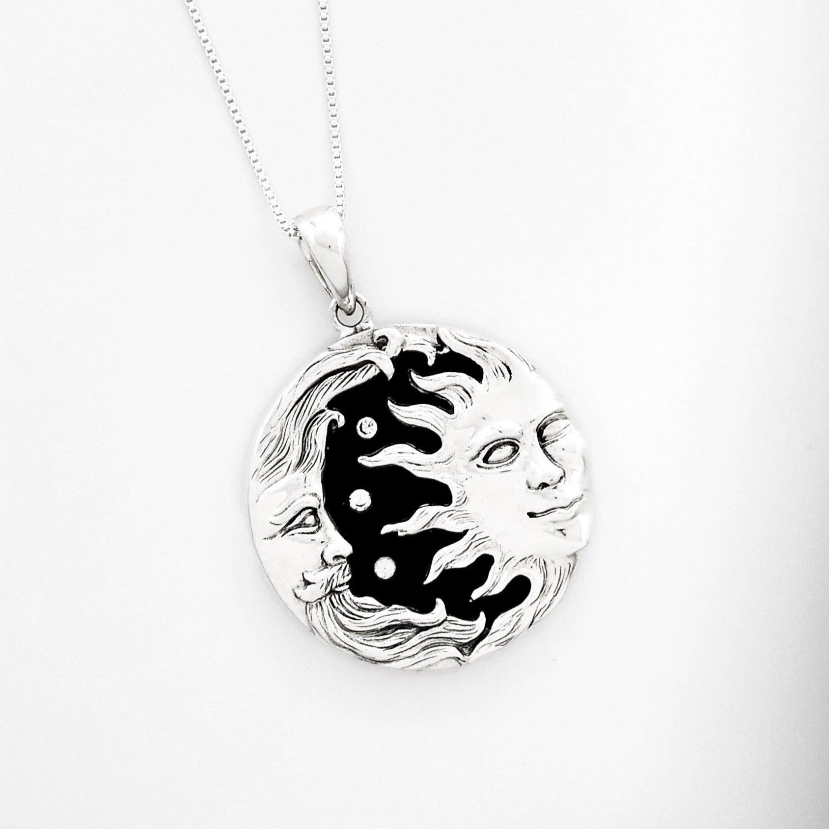 silver crescent moon with face and beard looking towards a half sun with face and rays extending towards the moon. Three small cubic zirconiums sit between them. Black onyx is the background.