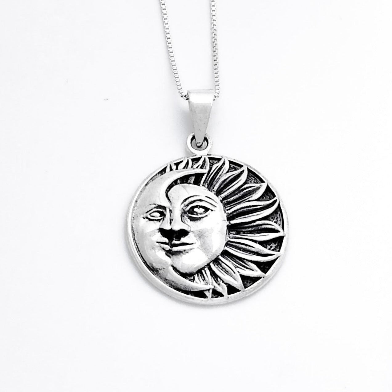 A circular pendant of a half sun with a face and 13 flower-petal-like rays extending to the right. A crescent moon with a face covers the left side.