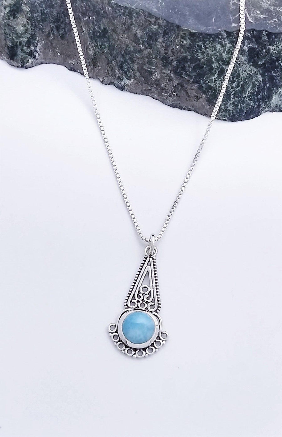 Sterling silver teardrop-shaped pendant with intricate details along the top half, with a large, Larimar stone at the bottom. Lining the bottom of the stone are eight silver circles. Comes on an 18-inch chain