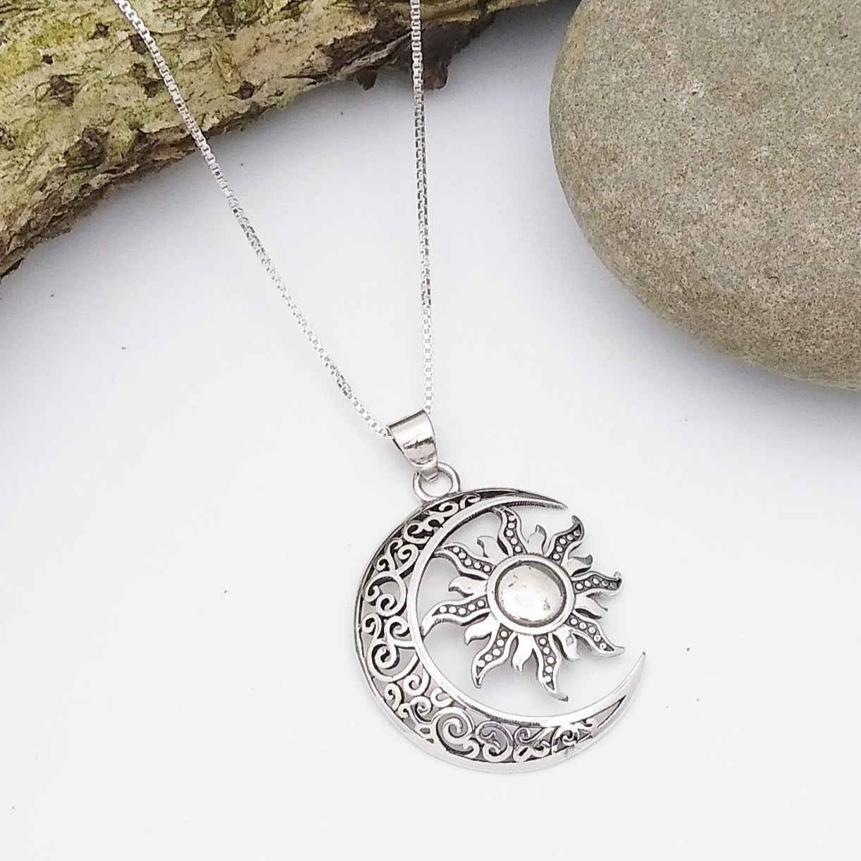 Sterling silver sun and moon pendant. The moon is a hollow crescent shape with simple designs in the metal work, and the sun has eight rays stretching out from the center with intricate designs in the metal.