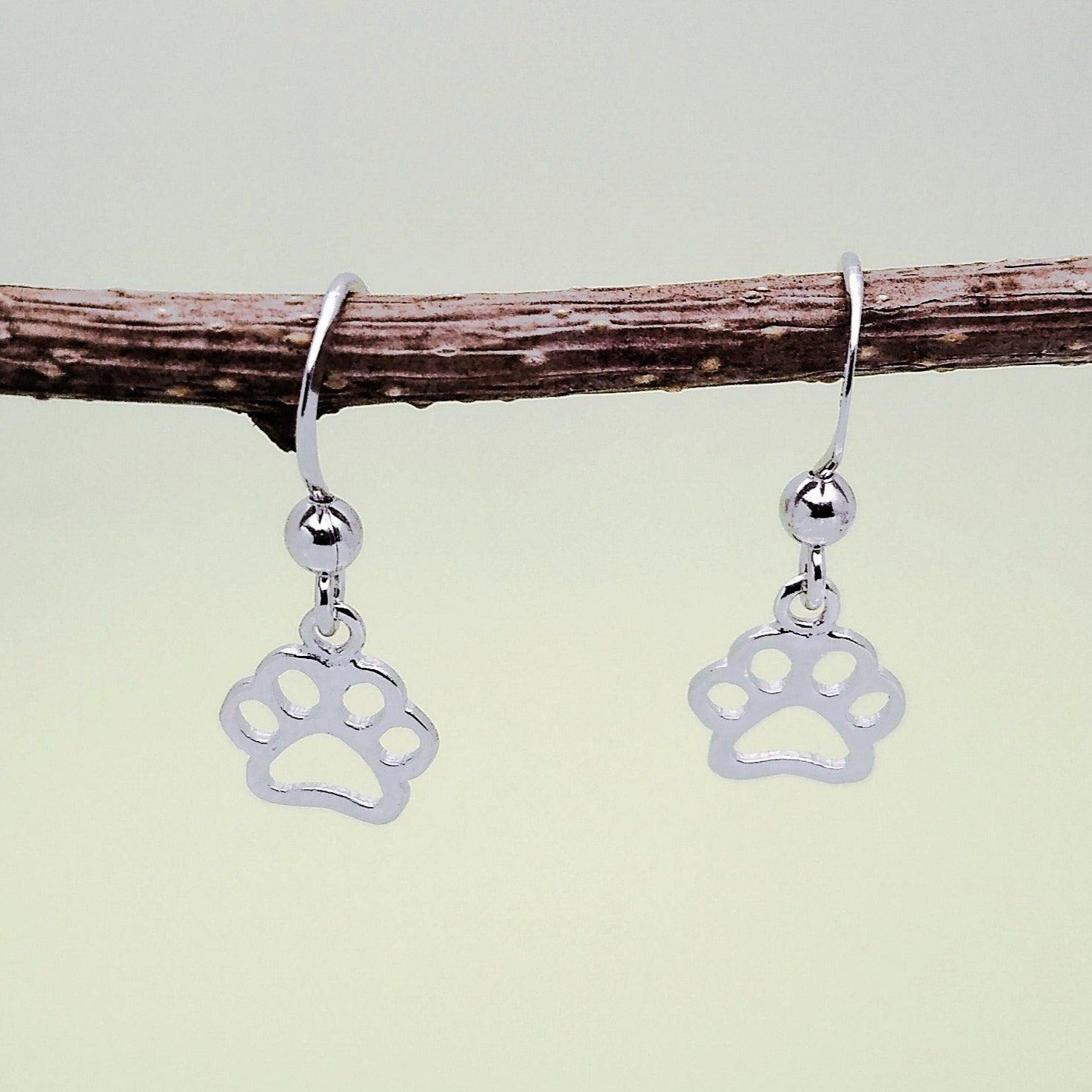 Sterling silver drop earrings of a paw print. Three are four toe cut outs above the bottom pad. Dangles from a French wire