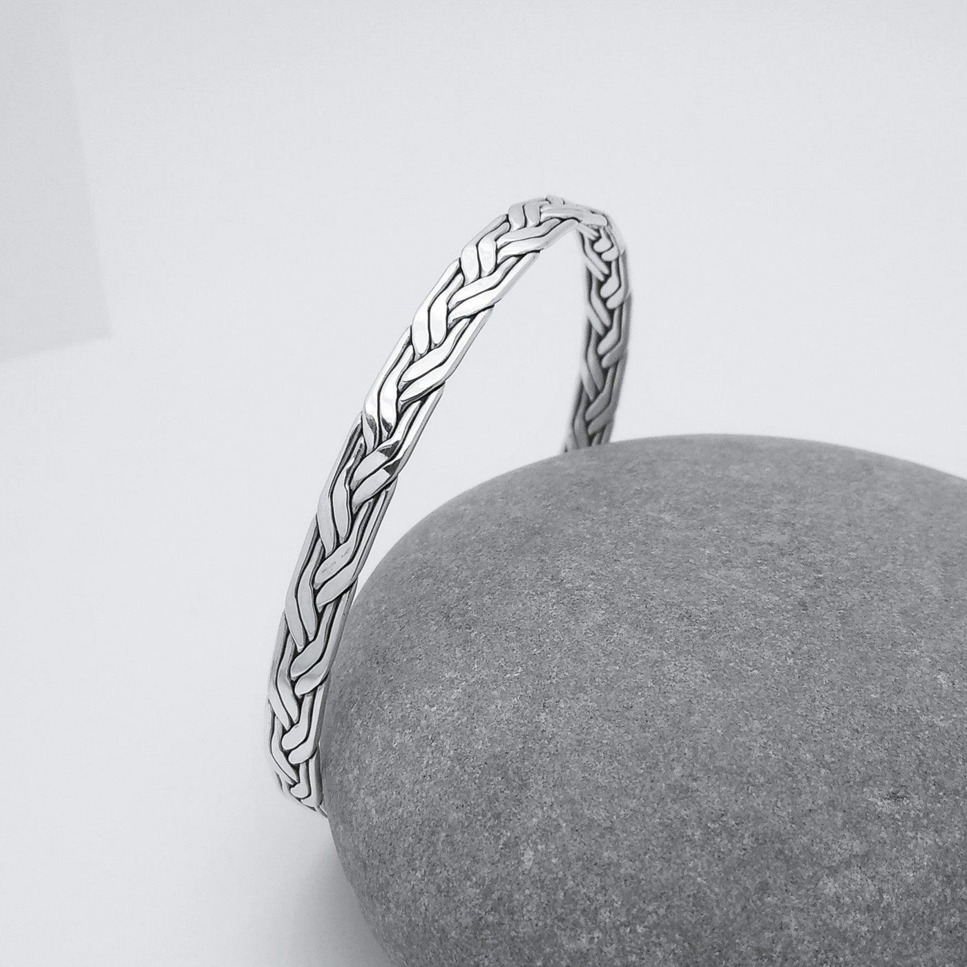 925 Sterling Silver 4 strand braided/woven bangle leaning against a small grey rock