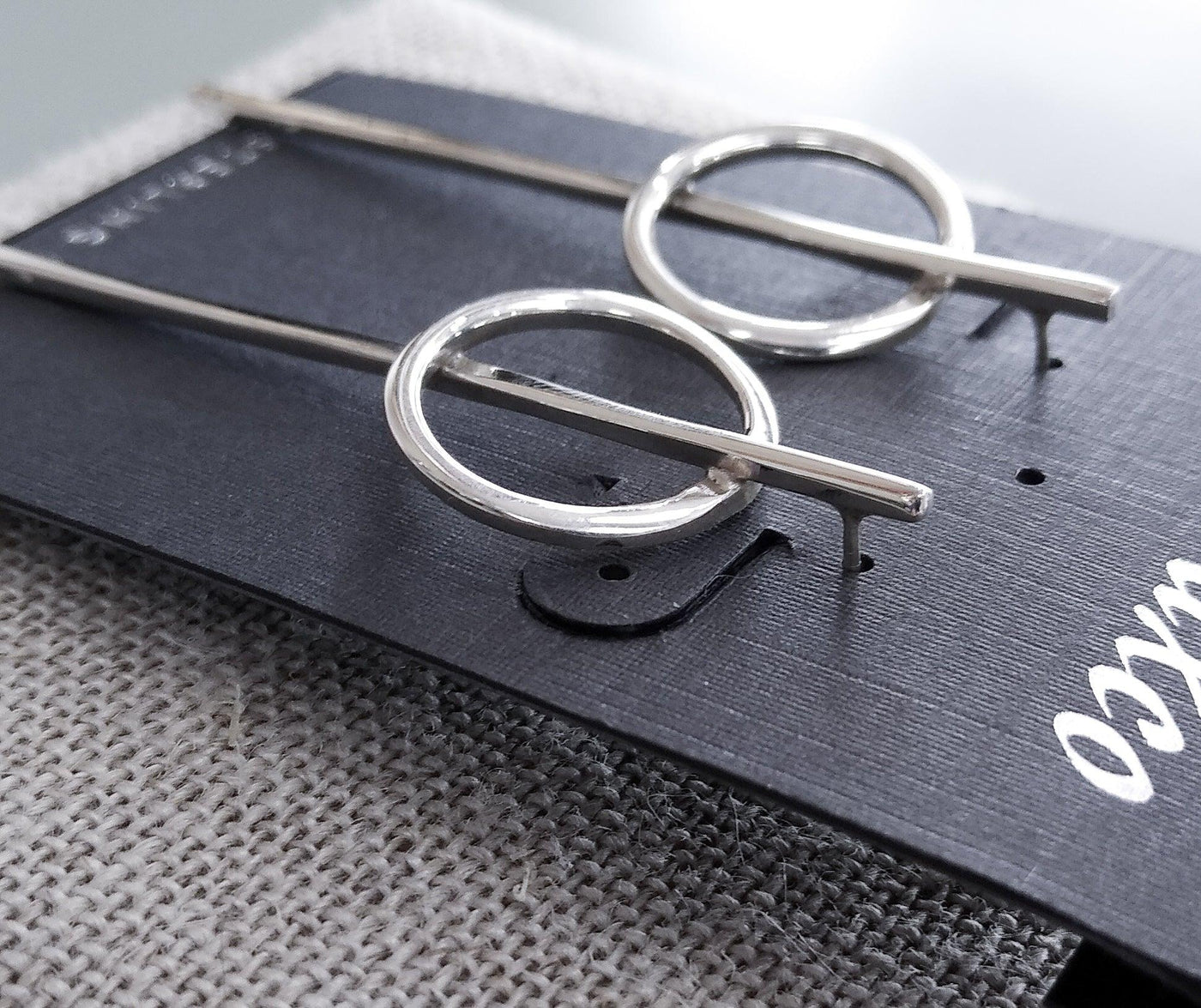 Side angle of the sterling earrings. A long, thin silver bar stretches through a circular hoop at the top of the earring.