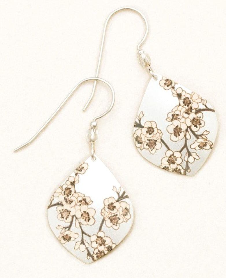 Diamond-shaped niobium earrings with white cherry blossoms on a pale off-white background. Sterling silver ear wire has a small bead at the bottom.