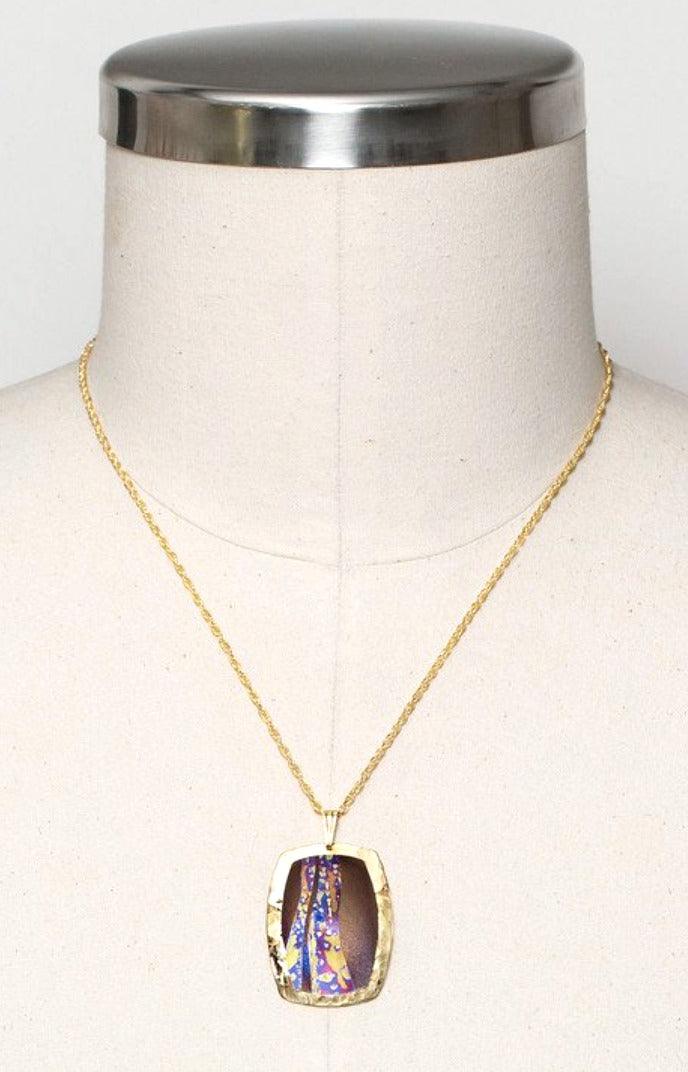 Rectangular sterling silver pendant with a purple/brown floral design in the middle. Hangs from an 18-inch gold-filled chain.