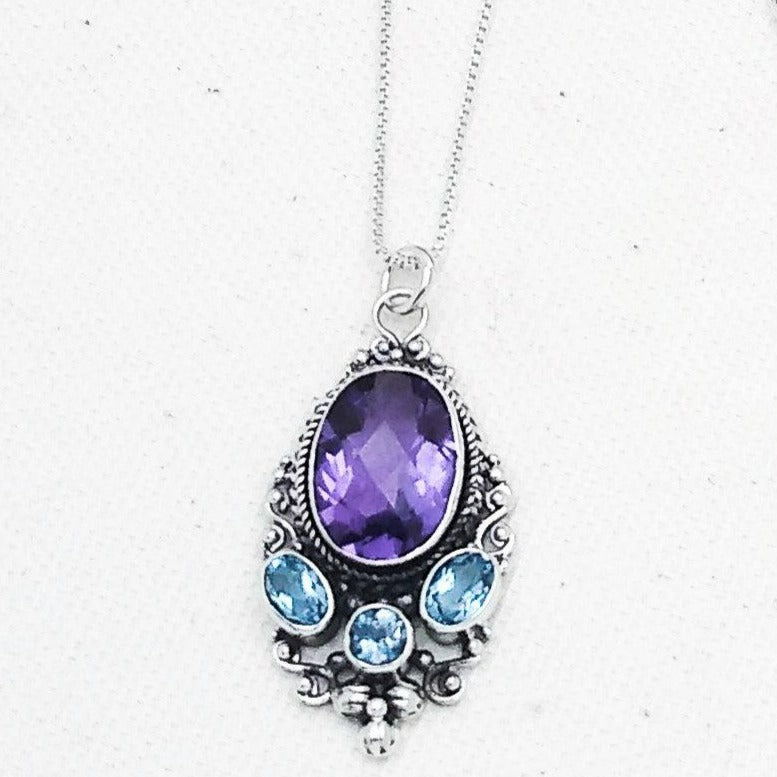 Beautiful sterling silver ovular pendant with an amethyst stone at the top, and three smaller blue topaz stones at the bottom surrounded by an ornate silver border. 18-inch chain