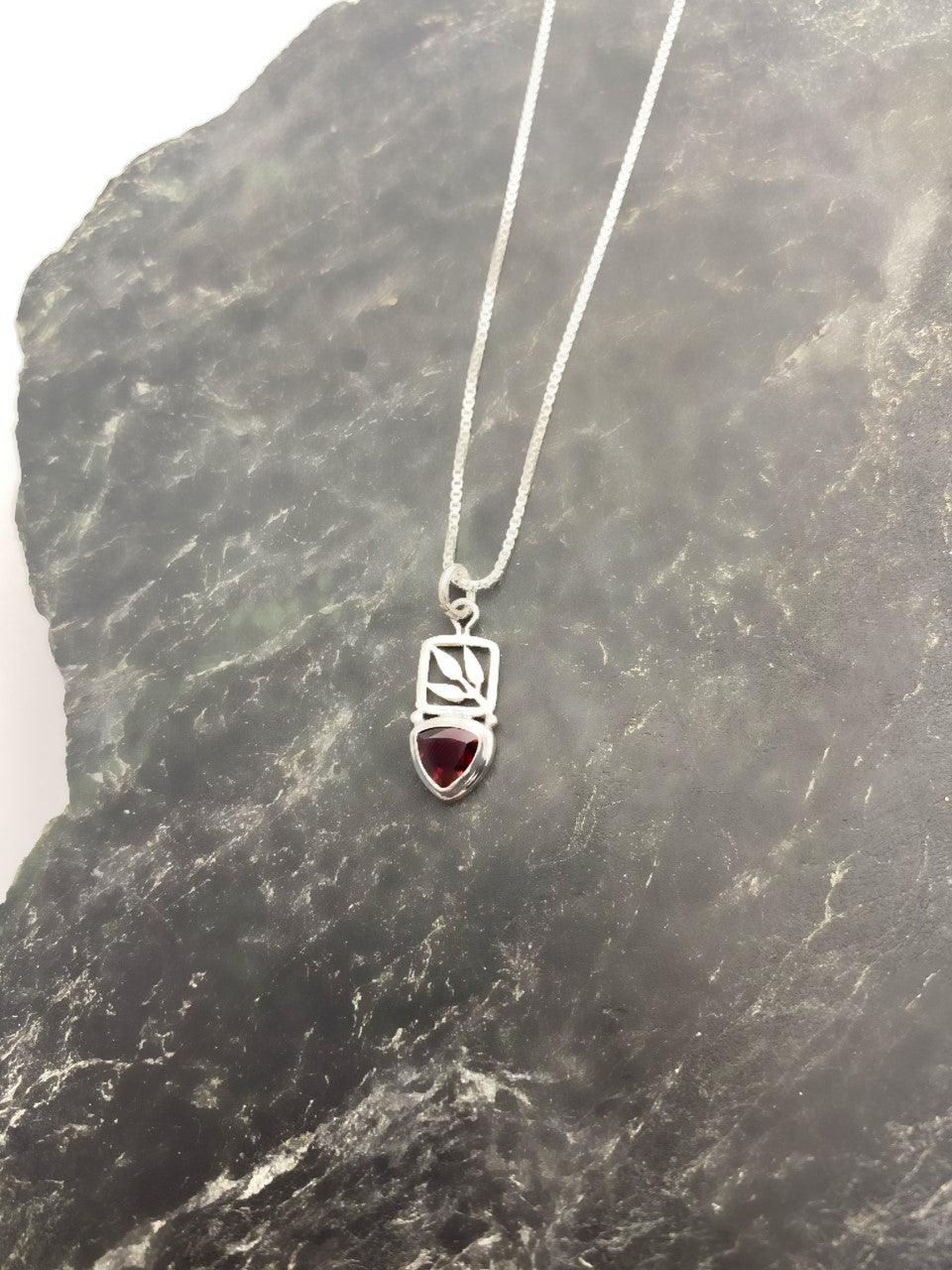 Sterling silver leaf cut out pendant with a small teardrop-shaped garnet stone at the bottom