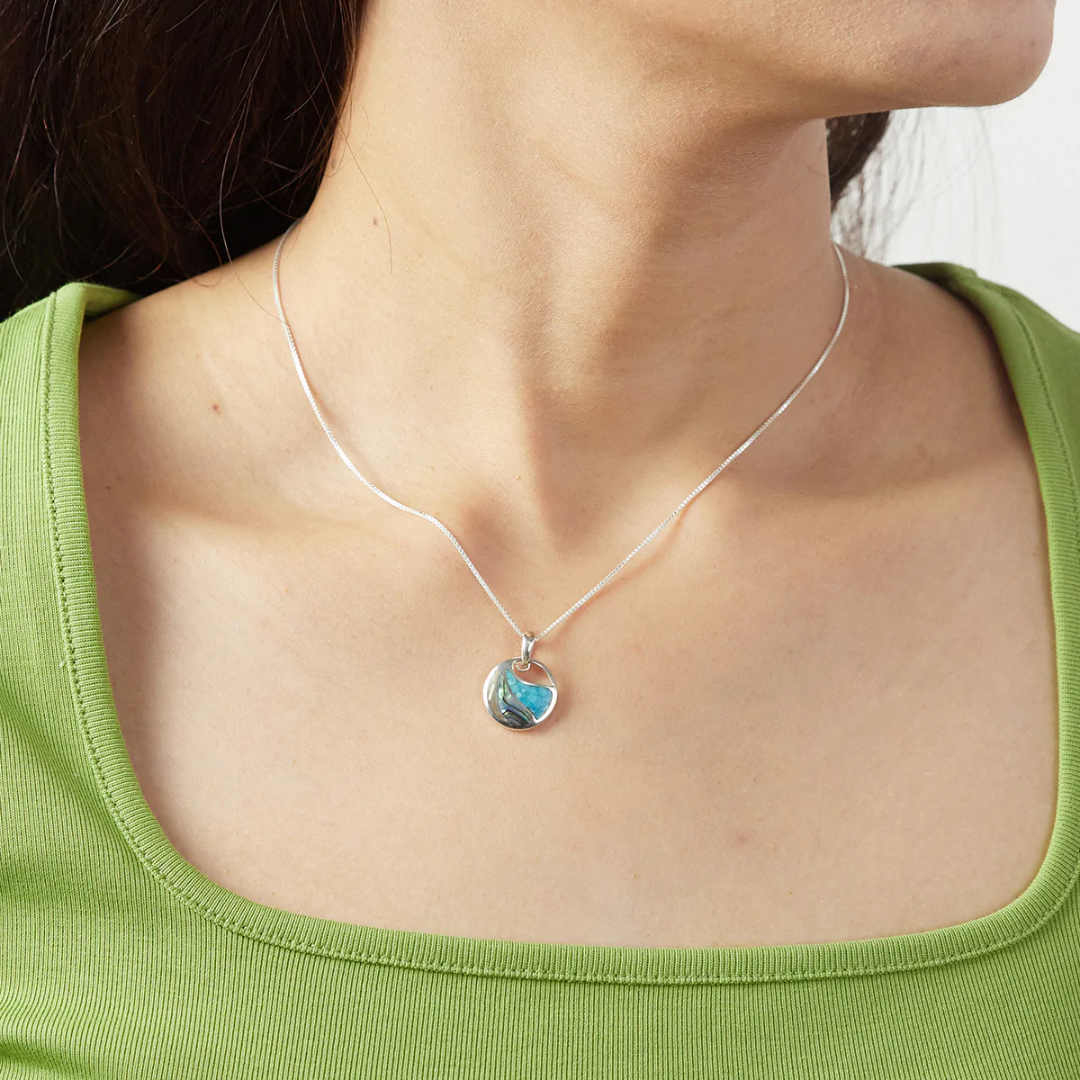 Sterling silver Boma circle with three separated sections of mosaic blue Mother of Pearl and Abalone with a cut-out at the top. Comes with 18-inch silver chain. Seen on woman with green shirt. 