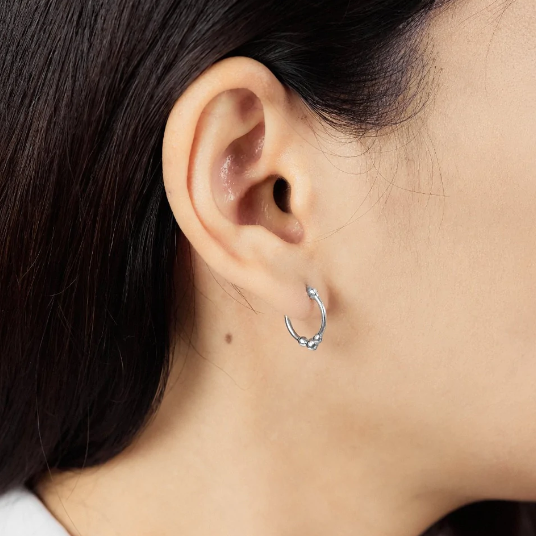 Snap top silver hoop with three small silver balls on the bottom, seen on human ear from side view. 