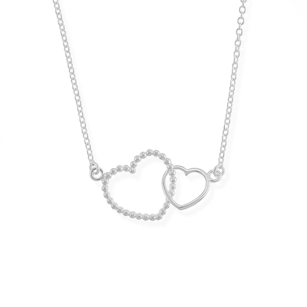 Interlocking heart necklace on white background, one heart bigger than the other, bigger heart is textured while smaller heart is smooth; on a thin silver chain.