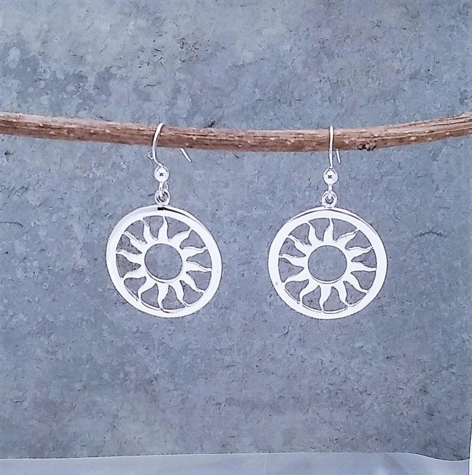 Sterling silver sun cut-out earrings on a French wire. 12 rays outstretch from a hollow center, surrounded by a simple sterling circle border.
